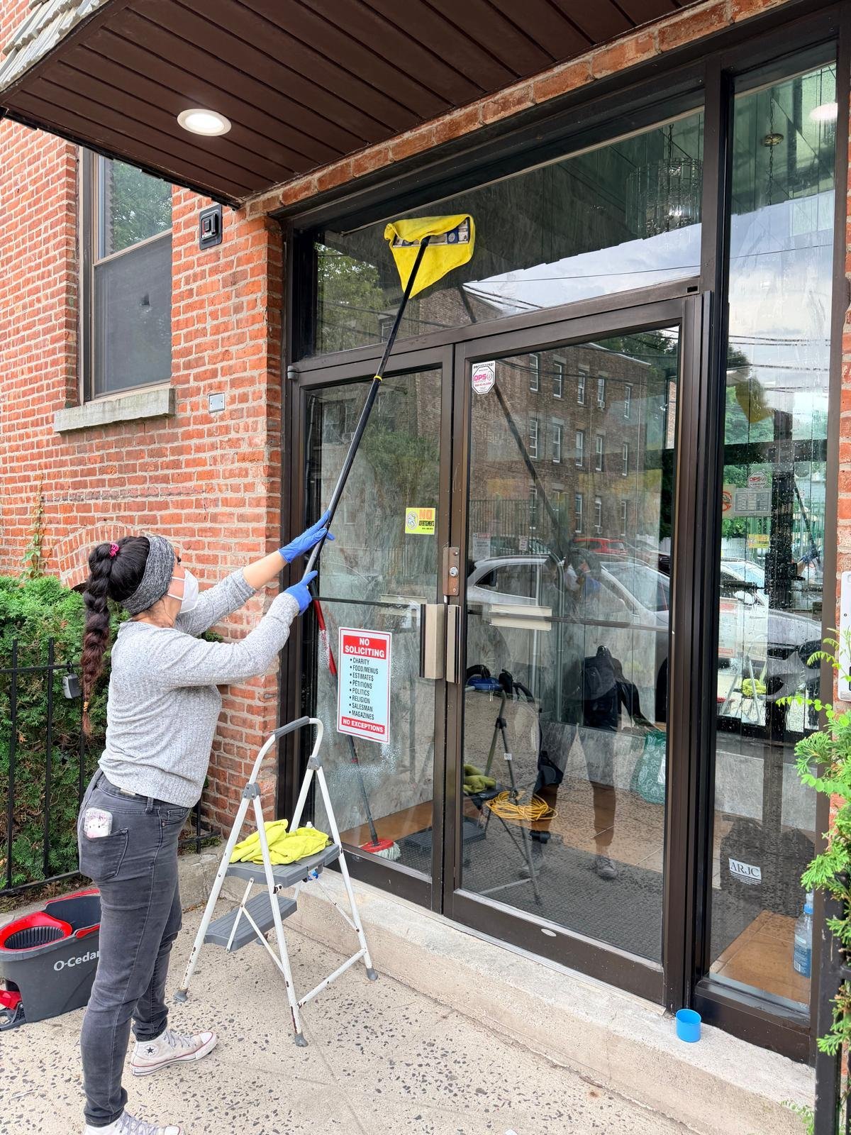 Worker cleaning large glass storefront doors and windows with professional equipment and ladder