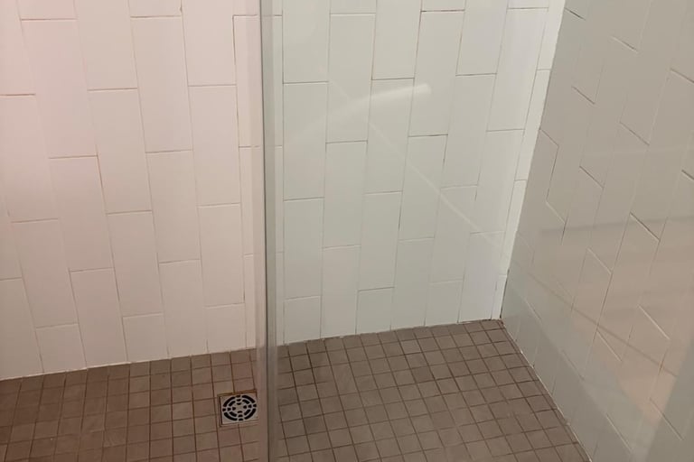 Empty bathroom shower stall with white subway tile walls, brown tile floor, and glass door panel