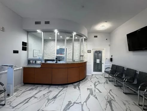 Modern medical office reception area with curved wooden counter, glass partition, marble flooring, and waiting chairs