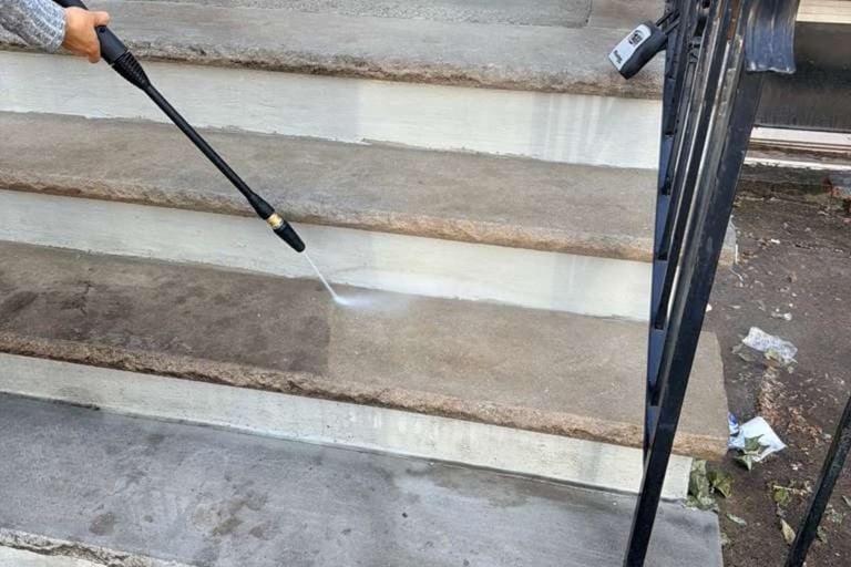 Someone using a pressure washer to clean concrete steps and sidewalk with a black wand spraying water
